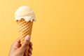 Hand holding vanilla milk ice cream cone on pastel background, a delightful summer treat