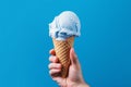 hand holding a waffle cone with white ice cream on a blue background, Generative AI