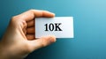 Hand Holding White Card with the Text 10K Isolated on a Blue Background, Representing Achievement. Royalty Free Stock Photo