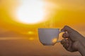 A Hand holding a white cup of hot espresso coffee mugs and nature view of the sun background in the morning with sunlight Royalty Free Stock Photo