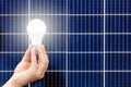 Hand holding white light bulb against solar panel, solar station. Idea concept of alternative energy, technology, environment, Royalty Free Stock Photo