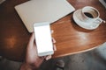 Hand holding white mobile phone with blank desktop screen with coffee cup and laptop on table Royalty Free Stock Photo