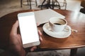 Hand holding white mobile phone with blank desktop screen with coffee cup and laptop on table Royalty Free Stock Photo