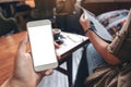 A hand holding white mobile phone with blank desktop screen and a woman reading magazine while sitting in cafe Royalty Free Stock Photo