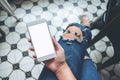 Hand holding white mobile phone with blank white screen on thigh with a vintage tile floor in cafe , feeling relaxed Royalty Free Stock Photo