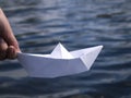 A hand is holding a white paper boat above the water. Royalty Free Stock Photo