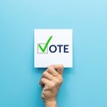 Hand holding white paper with the `vote` and green check mark voting symbols in checkbox of the inscription isolated on blue Royalty Free Stock Photo