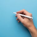 A hand holding a white pen is positioned against a solid blue background Royalty Free Stock Photo