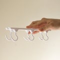 Hand holding white plastic hook rack organizer with rotating hooks. Household storage solution for kitchen, bathroom or closet. Royalty Free Stock Photo
