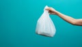 Hand holding a white plastic trash bag over a black bin with blue background Royalty Free Stock Photo