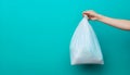 Hand holding a white plastic trash bag over a black bin with blue background Royalty Free Stock Photo