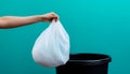 Hand holding a white plastic trash bag over a black bin with blue background Royalty Free Stock Photo