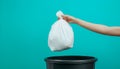Hand holding a white plastic trash bag over a black bin with blue background Royalty Free Stock Photo
