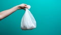 Hand holding a white plastic trash bag over a black bin with blue background Royalty Free Stock Photo