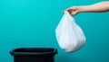 Hand holding a white plastic trash bag over a black bin with blue background Royalty Free Stock Photo