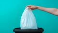 Hand holding a white plastic trash bag over a black bin with blue background Royalty Free Stock Photo