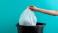 Hand holding a white plastic trash bag over a black bin with blue background Royalty Free Stock Photo
