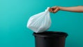 Hand holding a white plastic trash bag over a black bin with blue background Royalty Free Stock Photo