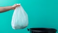 Hand holding a white plastic trash bag over a black bin with blue background Royalty Free Stock Photo