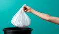 Hand holding a white plastic trash bag over a black bin with blue background Royalty Free Stock Photo