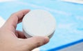 Hand holding a white rounded chlorine tablet.