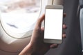 A hand holding a white smart phone with blank desktop screen next to an airplane window Royalty Free Stock Photo