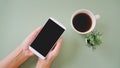 Hand holding white smartphone with clipping path on touchscreen, top view and blurred fake small tree and cup of coffee