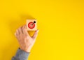 Hand holding wooden block with dartboard with arrow on yellow background