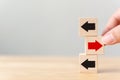 Hand holding wooden block with red arrow facing the opposite direction black arrows, Unique, think different