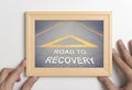 Hand holding wooden frame with road to recovery concept