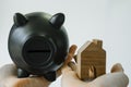 hand holding wooden miniature house and black piggy bank as financial saving or mortgage house loan concept Royalty Free Stock Photo