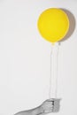 Hand holding yellow balloon on white wall