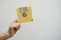 A hand holding a yellow floppy disk on a white background.