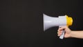 Hand is holding yellow megaphone on black background