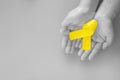 Hand holding Yellow ribbon on black and white background, copy space. Bone cancer Sarcoma Awareness childhood cancer Royalty Free Stock Photo