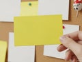 Hand holding a yellow sticky note with other notes and a wooden figure in the background Royalty Free Stock Photo