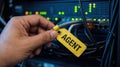 Hand holding yellow tag labeled AGENT on server cable in data center Concept of IT security, network management, and technology Royalty Free Stock Photo