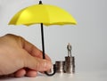 A hand holding a yellow umbrella and a miniature man standing on a pile of coins. Royalty Free Stock Photo