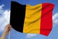 Hand holds against the background of the sky with clouds the colored flag of Belgium on the texture of the fabric, silk with waves Royalty Free Stock Photo