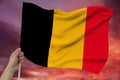 Hand holds against the background of the sky with clouds the colored flag of Belgium on the texture of the fabric, silk with waves Royalty Free Stock Photo