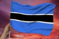 Hand holds against the background of the sky with clouds the colored flag of Botswana on the texture of the fabric, silk with