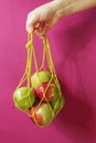 Hand holds a bag of string bag with ripe apples on a pink background. Eco-friendly packaging. Reusable Royalty Free Stock Photo