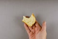 A hand holds a bitten half of a slice of wheat bread. A adult ma