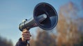 A hand holds a black megaphone against a blue sky with trees blurred in the background Royalty Free Stock Photo