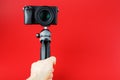 A hand holds a black SLR camera on a tripod, isolated on a red background Royalty Free Stock Photo