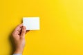 A hand holds a blank white notecard against a vibrant yellow background Royalty Free Stock Photo
