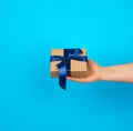 Hand holds a box with a gift wrapped in brown kraft paper and tied with a silk blue ribbon Royalty Free Stock Photo