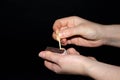 A hand holds a burning match on a black background. A wooden match burns in the hands of a macro. Igniting a match on a box. Smoke