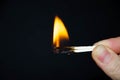 A hand holds a burning match on a black background. A wooden match burns in the hands of a macro. Igniting a match on a box. Smoke