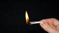 A hand holds a burning match on a black background. A wooden match burns in the hands of a macro. Igniting a match on a box. Smoke Royalty Free Stock Photo